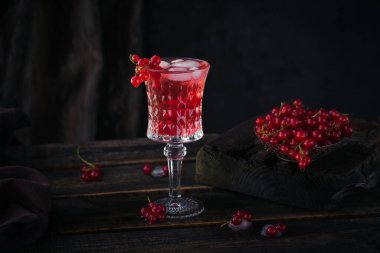 Bir bardak kırmızı frenk üzümü kokteyli ya da moktail, ezilmiş buzlu ferahlatıcı yaz içeceği ve koyu ahşap arka planda köpüklü su..