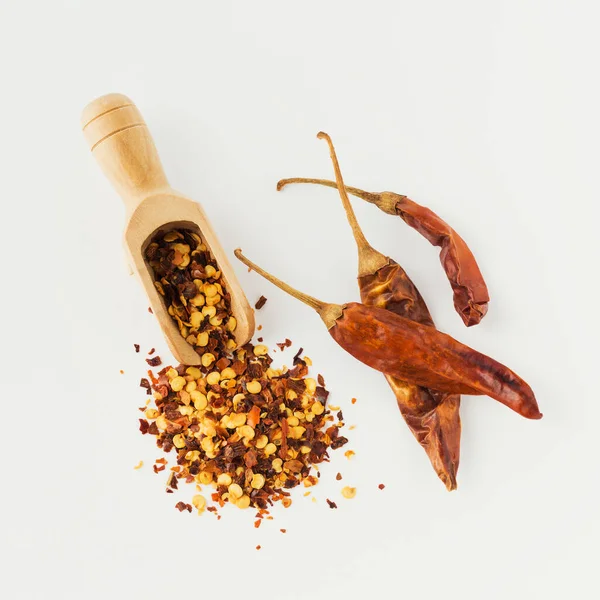 Wooden scoop full of crushed red cayenne pepper, dried chili flakes and seeds isolated on white background. Homemade spices ingredients for cooking.