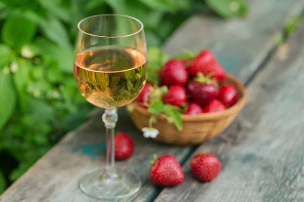 A glass of rose wine served with fresh strawberries on wooden background. Summer picnic outdoor with pink wine and berries.