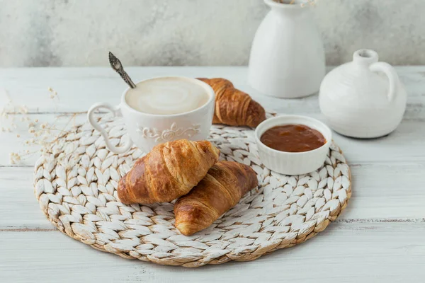 Heerlijk ontbijt met verse croissants en een kop koffie geserveerd met jam op een witte houten achtergrond. Heerlijk bakken — Stockfoto