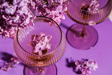 Lacivert çiçeklerle dolu şampanya kadehleri yumuşak doğal ışıklandırmada, pastel arka planda, yemyeşil mor çiçeklerin arasına yerleştirilir.