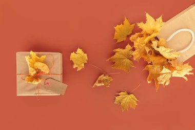 Sonbahar yaratıcı tatil hediyesi. El yapımı kağıt hediye kutusu ve turuncu masanın üzerinde yapraklar var. Hediye paketi. Şükran Günü, sonbahar tatili, sonbahar geçmişi