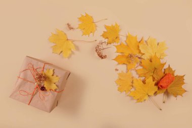 Sonbahar yaratıcı tatil hediyesi. El yapımı kağıt hediye kutusu ve bej masa üzerinde yapraklar. Hediye paketi. Şükran Günü, sonbahar tatili, sonbahar geçmişi