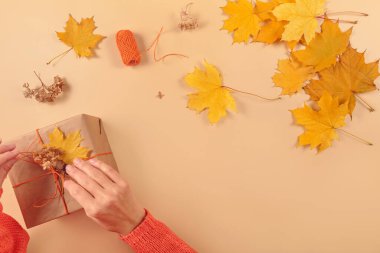 Autumn creative holiday present. Handmade paper gift box with foliage dried leaves on yellow table. Thanksgiving day, autumn holidays, fall background