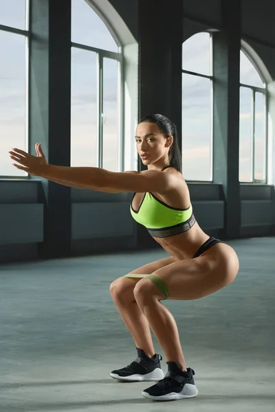 Aantrekkelijke vrouw met atletisch lichaam doen zittend en downs in ruime sportschool. — Stockfoto