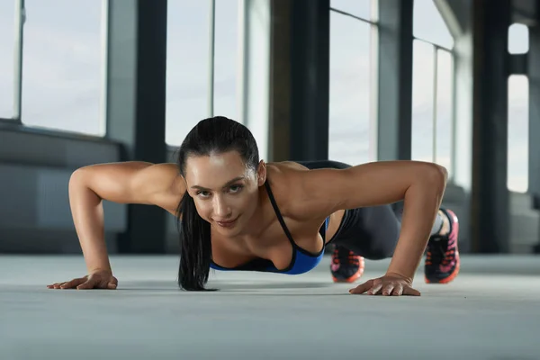 Sportig tjej med atletisk kropp göra push ups på golvet gym. — Stockfoto