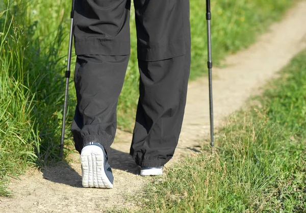 Ο άνθρωπος περπατώντας στην αμμώδη διαδρομή φοράει αθλητικά, χρησιμοποιώντας τα ραβδιά παρακολούθησης. — Φωτογραφία Αρχείου