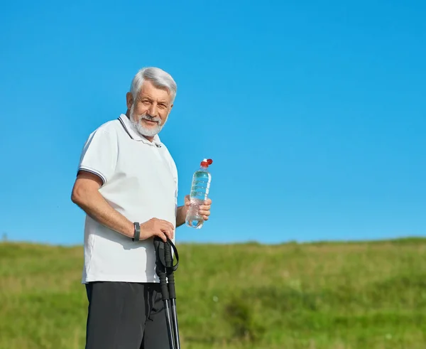 Old man keeping water bottle and tracking sticks. — Stock Photo, Image