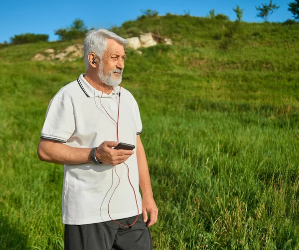 Old man keeping cellphone, running on countryside.