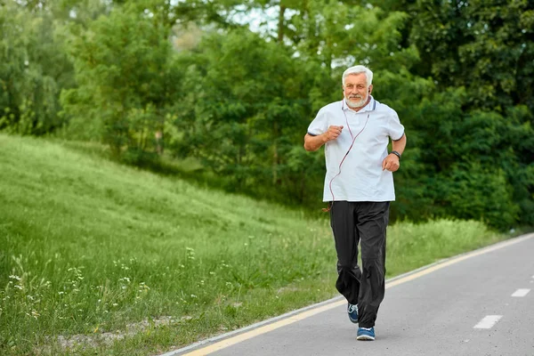 Adatto al vecchio che corre in pista nel parco verde . — Foto Stock