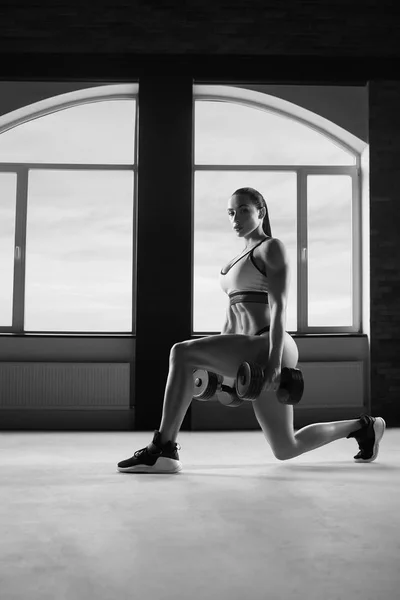 Черно-белое фото сильной женщины, делающей упражнения с гантелями . — стоковое фото