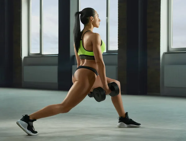 Sideview of athletic girl performing fallouts with dumbbells. — Stock Photo, Image