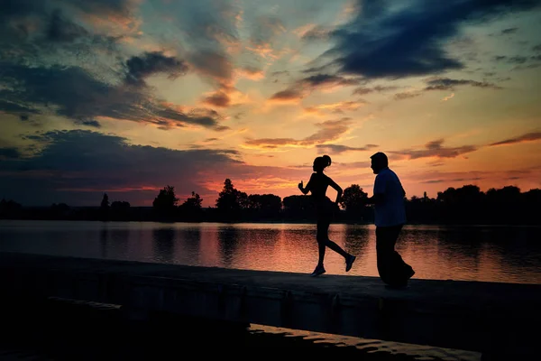 Ciemne sylwetki dziewczyna i starszy człowiek pracy podczas zachodu słońca w pobliżu jeziora. — Zdjęcie stockowe