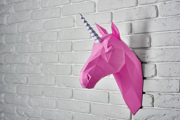 Gesättigter rosafarbener Einhörnerkopf aus Papier, der an einer weißen Ziegelwand hängt. — Stockfoto