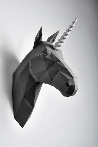 Black geometrical unicorns head paper hanging on grey shadowed wall.