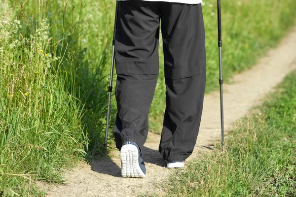 Περπάτημα άνθρωπος στο πράσινο πεδία αμμώδη διαδρομή, χρησιμοποιώντας τα ραβδιά παρακολούθησης. — Φωτογραφία Αρχείου