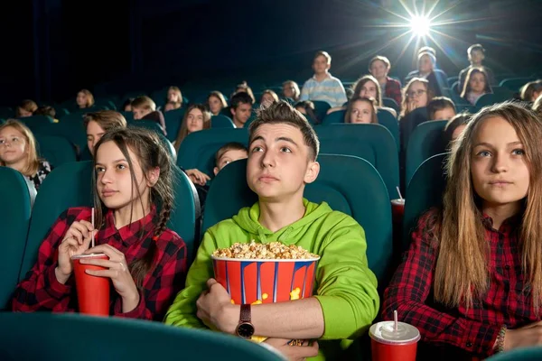 Teenagers eating popcorn and watching film in cinema.