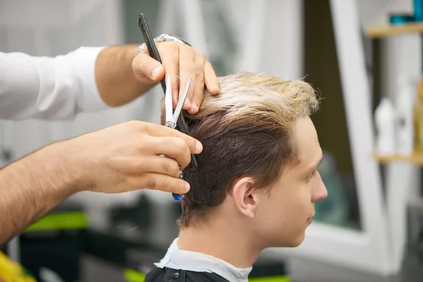 Закрытие рук парикмахеров, делающих новую стрижку для молодого клиента . — стоковое фото