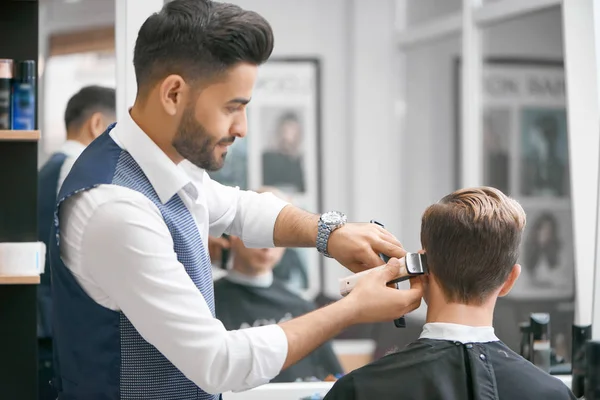 Barber doing new haircut for young client sitting in front of mirror.