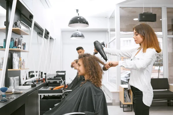 Female hairstylist drying curly girls hair using big plastic brush. — Stock Photo, Image