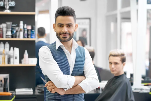 Симпатичный парикмахер, позирующий перед молодым клиентом, сидящим у зеркала . — стоковое фото