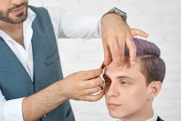 Парикмахер делает стрижку для молодого клиента с сиреневыми волосами . — стоковое фото