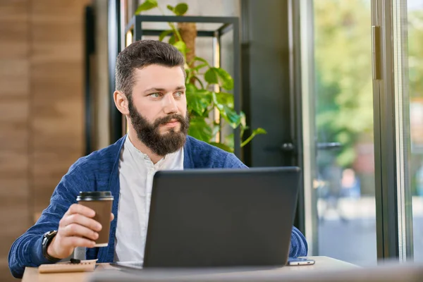 Homem atraente com barba e olhos azuis trabalhando com laptop . — Fotografia de Stock