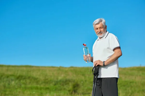 Old man keeping water bottle and tracking sticks. — Stock Photo, Image