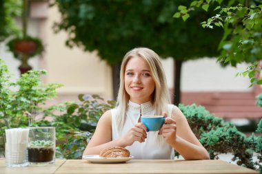 Kahve içme, kruvasan yiyorsun açık havada kafe lodge üzerinde oturan güzel kız.