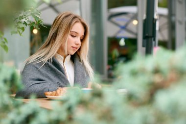 Genç sarışın kız kitap oturma okuma yan görünüm battaniye ile örtülü.