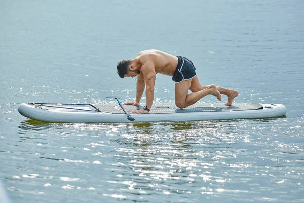 Uygun adam sup tahta üzerinde oturan fitness egzersizleri yapıyor yan görünüm. — Stok fotoğraf