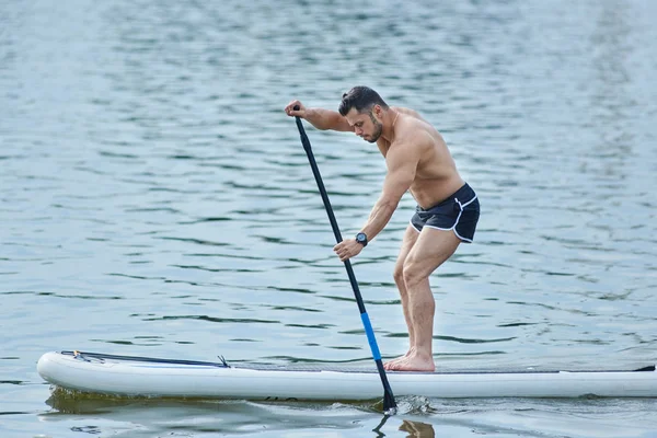 Vista lateral del entrenamiento del hombre con sup board, roaming con charco largo en el lago de la ciudad . — Foto de Stock