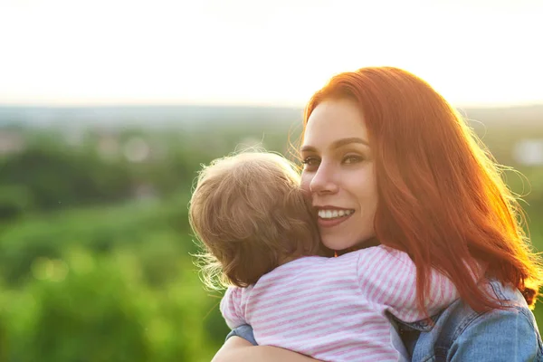 Ung mamma kramar barn, leende på vacker panoramautsikt bakom. — Stockfoto