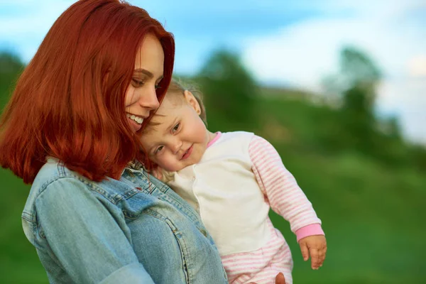 Vista laterale della madre mantenendo carino bambino in posa sul campo verde . — Foto Stock