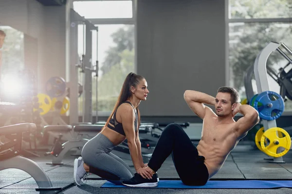 Mujer sosteniendo hombre pies abajo como él haciendo sentarse hasta ejercicios . — Foto de Stock