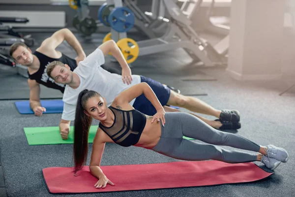 Drei junge Leute üben sich beim Yoga im Fitnessstudio in Seitenplankenpositionen. — Stockfoto