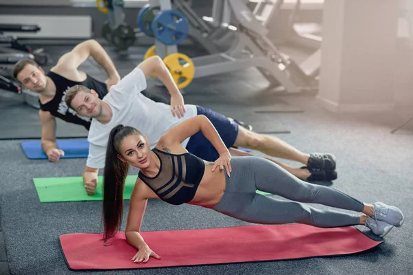 Tres jóvenes practicando postura lateral durante el yoga en el gimnasio . — Foto de Stock