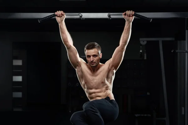 Muskuløs mannlig idrettsutøver som kjører opp på horisontal stang i mørk gymsal . – stockfoto