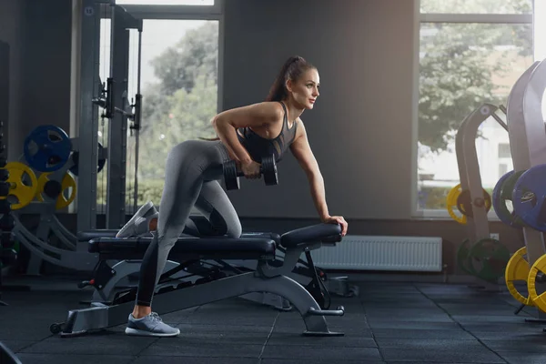 Sexy atletische vrouw oppompen van spieren met halters op sportschool. — Stockfoto