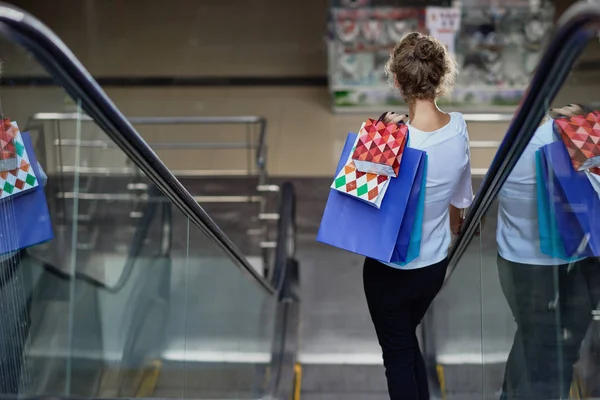 View from back of customer with shopping bags driving down on escalator in mall — Stock Photo, Image