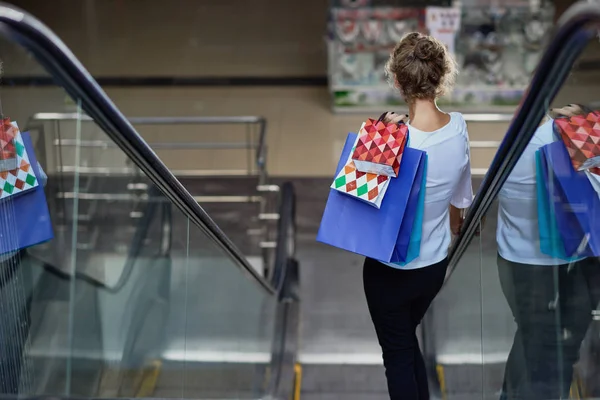 View from back of customer with shopping bags driving down on escalator in mall