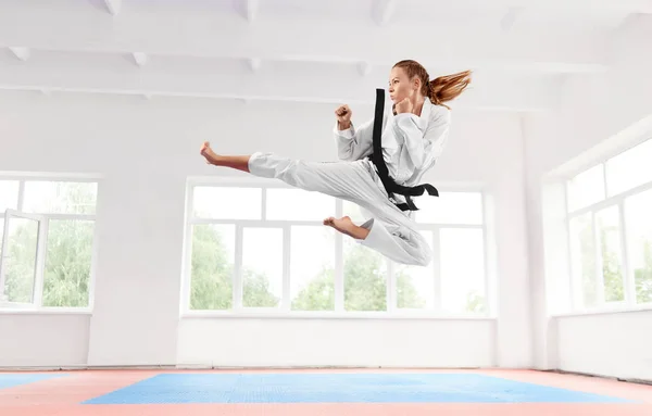 Mulher de quimono branco com cinto preto pulando e executando chute . — Fotografia de Stock