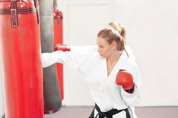 Two strong women boxing red heavy bag in gym.