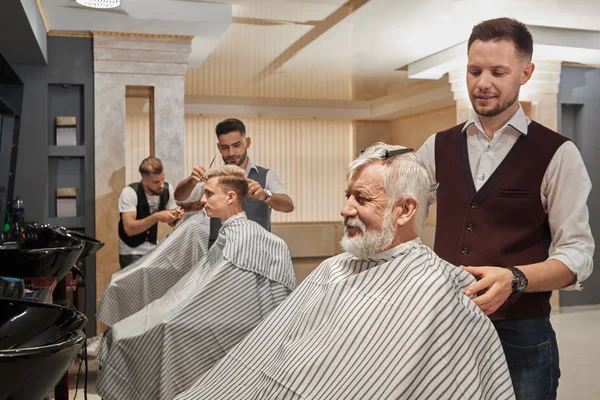 Trois coiffeurs coupant et toilettant les cheveux des clients . — Photo