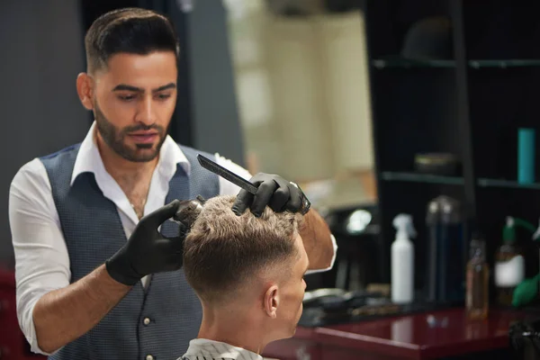 Hairdresser looking at client and trimming his haircut.