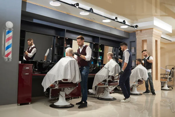 Barbiers travaillant avec des clients dans le salon de coiffure moderne . — Photo