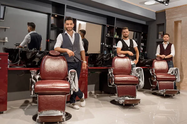 Maîtres confiants coiffeurs debout près des chaises de coiffeur et posant . — Photo