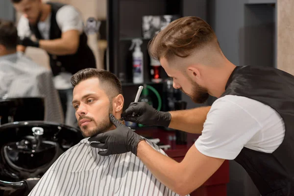 Парикмахер сконцентрировался на бритье бороды мужчин с помощью острой бритвы . — стоковое фото