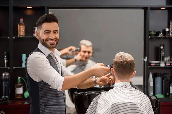 Souriant coiffeur rognant clients coiffure élégante et regardant la caméra . — Photo