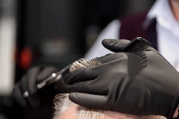 Barbiers mains en gants noirs faisant coupe de cheveux avec peigne et ciseaux . — Photo